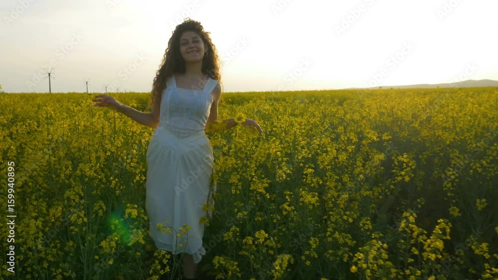 Pretty girl with white dress walking towards camera in field of rapeseed yellow flowers Pretty girl with white dress walking towards camera in field of rapeseed yellow flowers