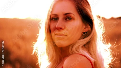 Beautiful blond woman in a red dress, on a wheat field at sunset