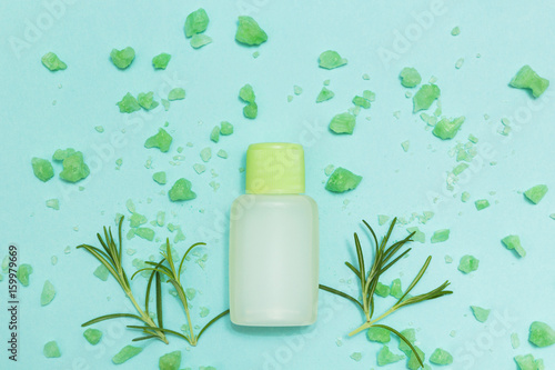 A bottle of essential oil and salt with fresh herb rosemary on a blue background. Top view.