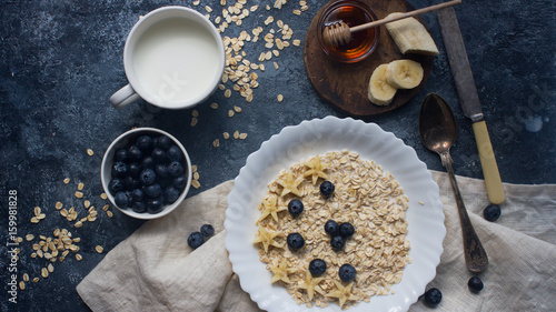 Organic oatmeal porridge with blueberry, banana, honey and milk on dark stone table, healthy lifestyle and diet concept, natural food, tasty breakfast, top view © Irina
