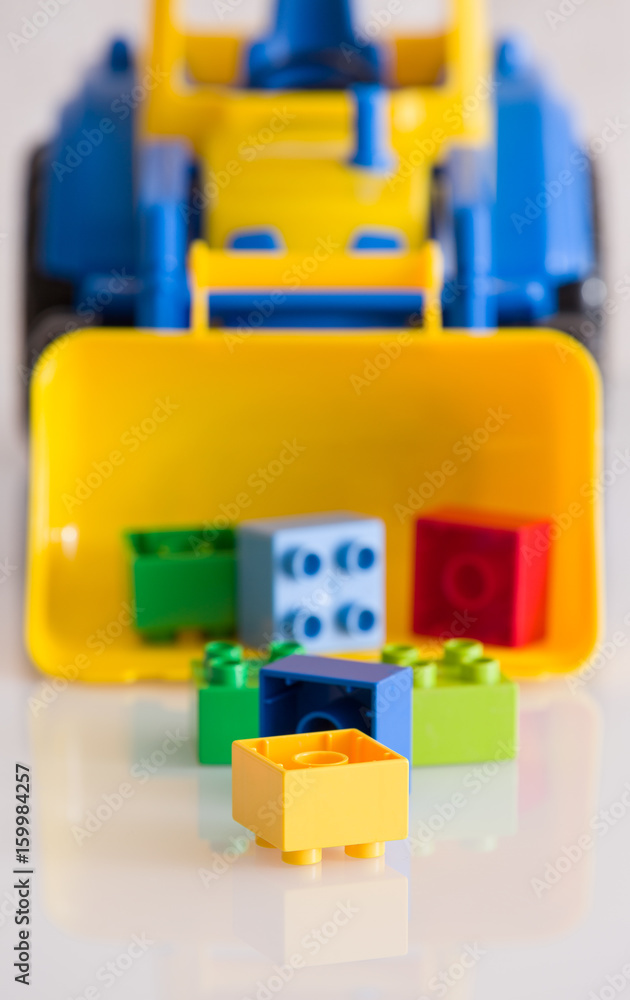 Fototapeta premium Closeup of children toy tractor with colorful plastic bricks or details on white background. Baby's toys on the table isolated.