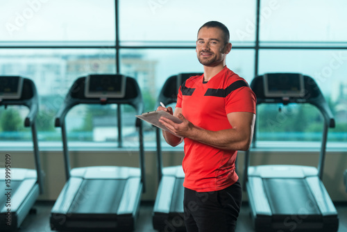 Personal Trainer Takes Notes On Clipboard In Gym