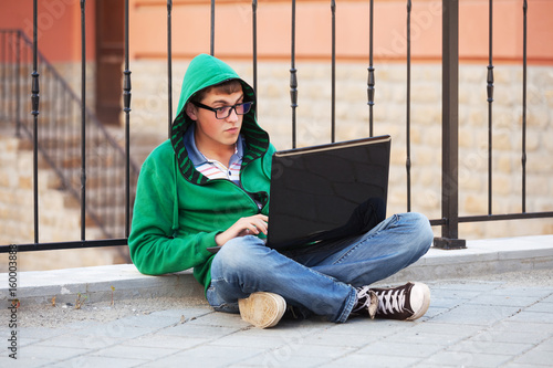 Young man using laptop on city street © Wrangler