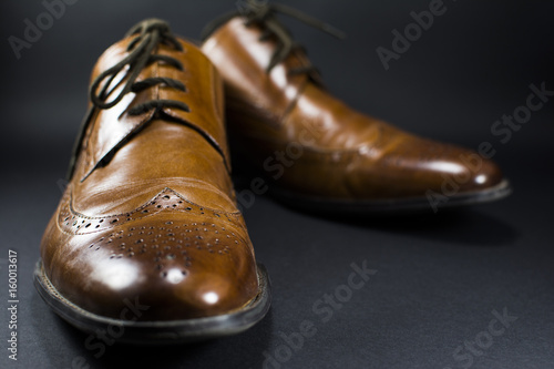 Beautiful brown leather men's shoes. Fashionable shoes isolated on black background. Lens flare in the background.