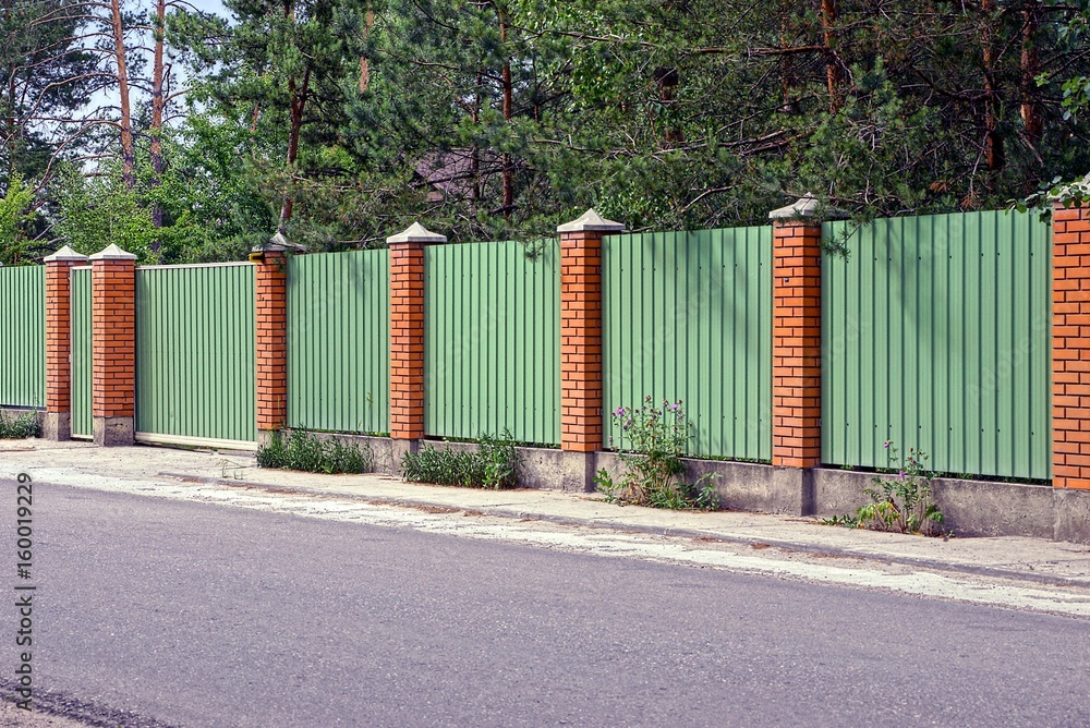зелёно коричневый забор и ворота перед асфальтированной дорогой