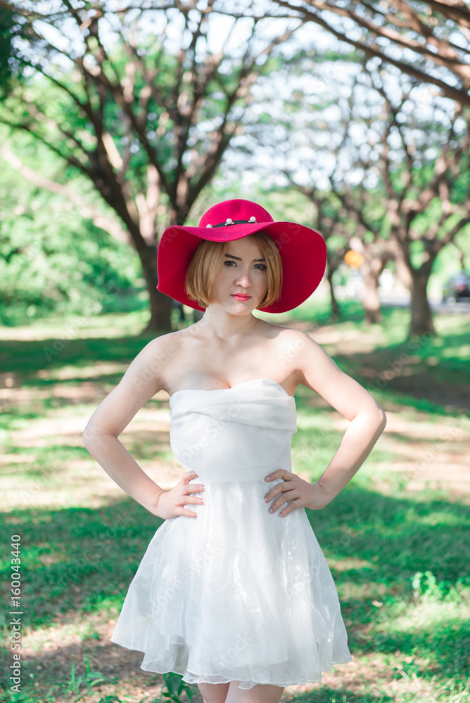 Portrait of Beautiful thai woman in white dress gold hairs wear red hat stand under tunnel tree in the sunny day,bright sunlight Portrait of Beautiful thai woman in white dress gold hairs wear red hat stand under tunnel tree in the sunny day,bright sunlight
