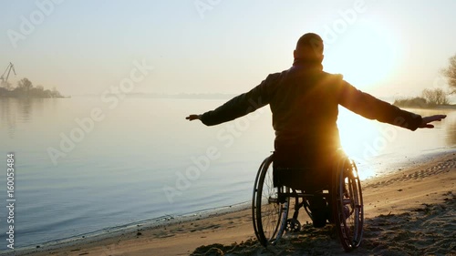 cripple person hands up, sundown on wheel chair, lonely disabled on wheelchair, male handicapped faith in future, self-confidence in human invalid, man outdoors, near river, back view
