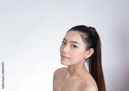 Portrait of a smiling young woman with natural make-up. beautiful asian girl standing against white background. Skincare, healthcare, studio shot.