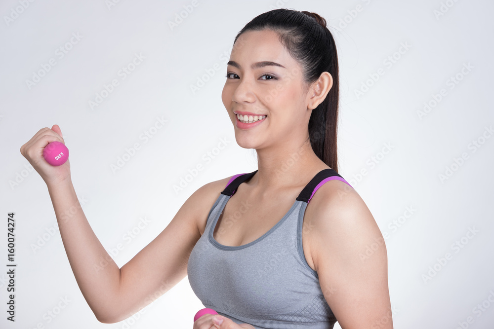 Young asian sporting woman training with dumbbell. Pretty athletic girl making physical exercise against white background. Healthy lifestyle concept. Young asian sporting woman training with dumbbell. Pretty athletic girl making physical exercise against white background. Healthy lifestyle concept.