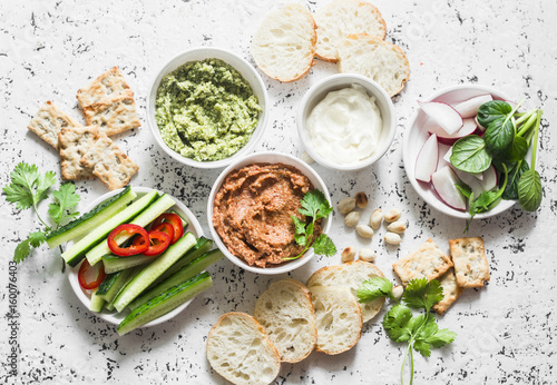 Vegetarian dip table. Eggplant, harissa, walnuts dip, broccoli dip, soft tofu and fresh vegetables on a light background, top view. Flat lay photo