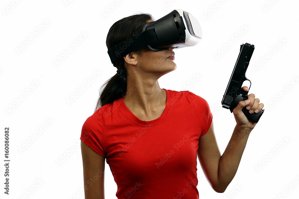 Young attractive woman in red shirt wearing virtual reality goggles holding gun Young attractive woman in red shirt wearing virtual reality goggles holding gun