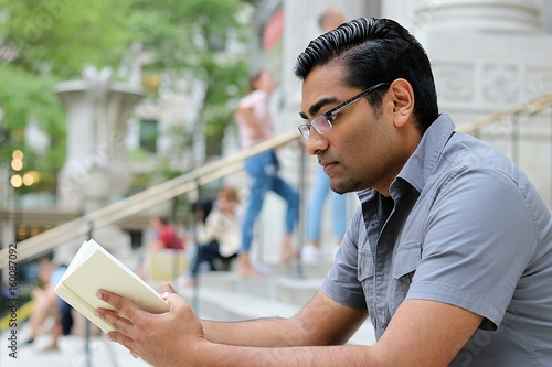 handsome young man reading a book on steps in a city location photo