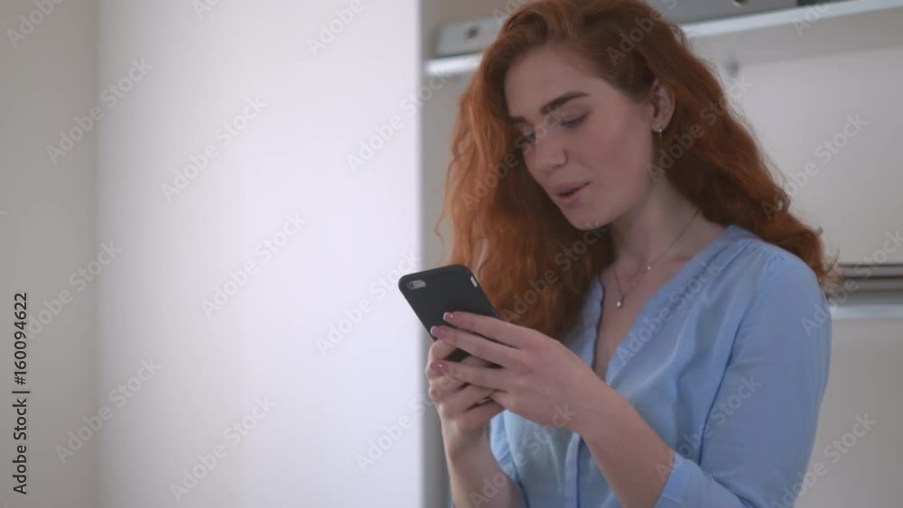 redheaded girl chatting smiling using smartphone. Woman with curly red hair using app on mobile phone for chatting in social net. redheaded girl chatting smiling using smartphone. Woman with curly red hair using app on mobile phone for chatting in social net.