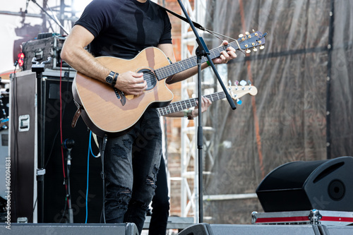 Behang musician playing acoustic guitar on outdoor stage during rock concert