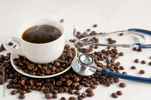 a cup of coffee ,coffee beans and stethoscope on white wooden background  in concept Health of coffee drinkers, quality of coffee