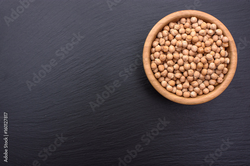 Peeled chickpeas lies in a wooden cup on a stony black board, black background, space for text