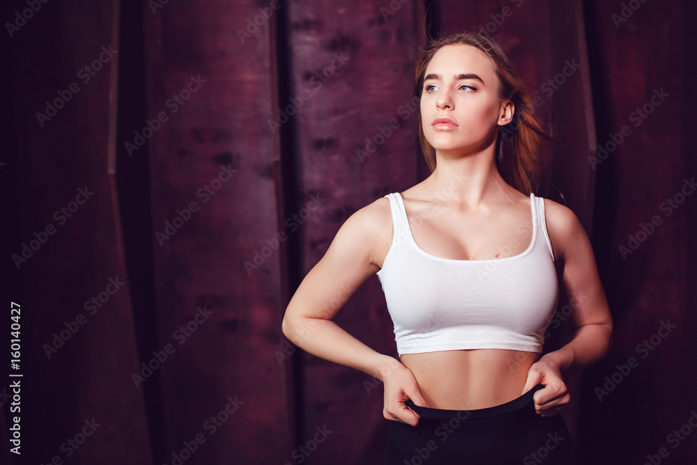 Sexy blonde woman with huge breast in a white tank top standing on a dark wooden wall background. Mock-up.