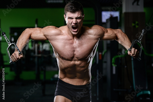 Muscular handsome athletic bodybuilder fitness model posing after exercises in gym on diet .