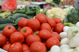 Pile of fresh tomatoes and other spring vegetables on a green market stall