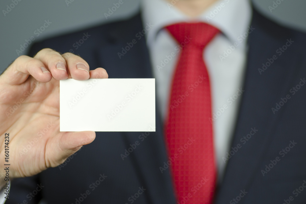 Close-up view of a manager's hand in a suit and with a red tie holding an empty white business card Close-up view of a manager's hand in a suit and with a red tie holding an empty white business card