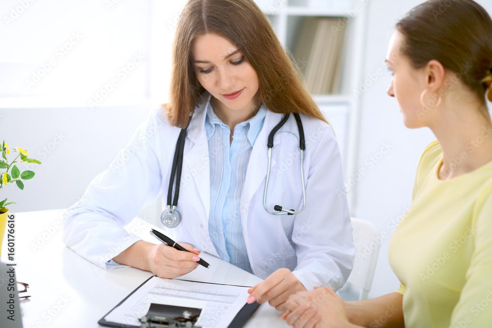 Doctor and patient have a talk while sitting at the desk near window Doctor and patient have a talk while sitting at the desk near window