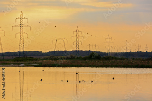 High-voltage poles reflected in the water of a lake