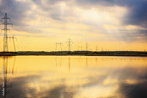 High-voltage poles reflected in the water of a lake