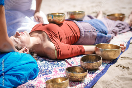 Beautiful female receiving energy sound massage with singing bowls and body massage on a river bank at spring sunny day
