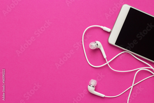studio shot of smartphone and earbuds on bright purple background
