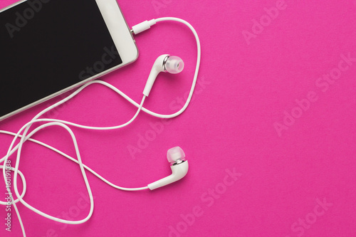 studio shot of smartphone and earbuds on bright purple background