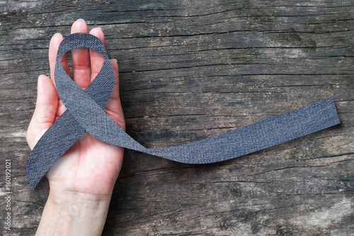 Blue jeans denim ribbon (isolated with clipping path) on helping hand support and aged wood for genetic disorder awareness and children's rare disease illness  photo