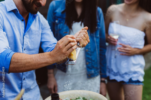 Man grates parmesan on salad at barbecue with friends