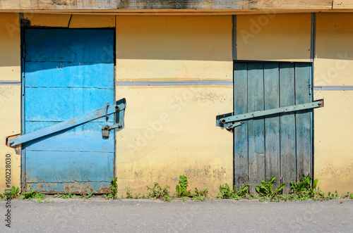 Fototapeta Naklejka Na Ścianę i Meble -  Yellow plastered facade with blue wooden doors. Yellow Wall Background