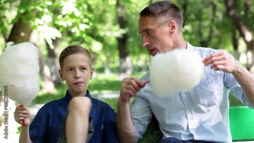 Father and son are resting in the park during the summer holidays and eat sweets, talk father and son about the Father's Day holiday