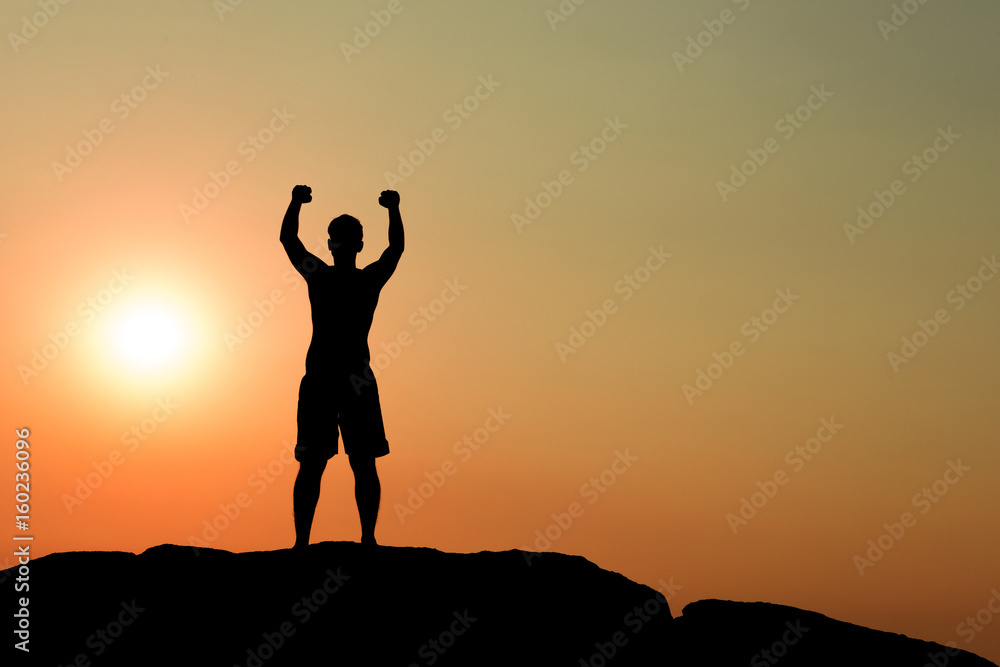 Silhouette of half naked confident man doing a winning pose against the sun on rocky ground