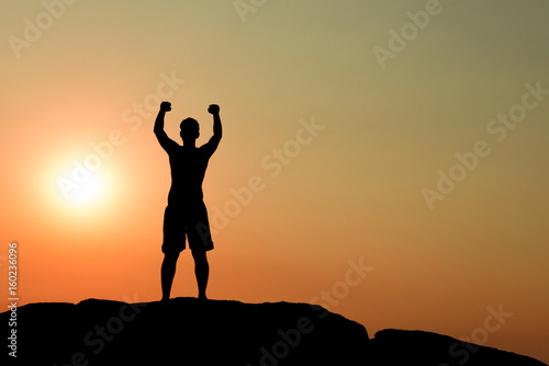 Silhouette of half naked confident man doing a winning pose against the sun on rocky ground © Baan Taksin Studio