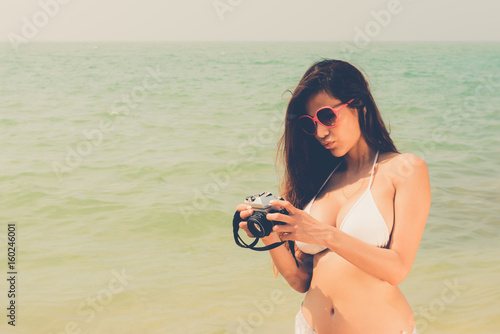 Beautiful attractive large breast asian bikini woman posing sexy portrait on beach holding vintage retro camera