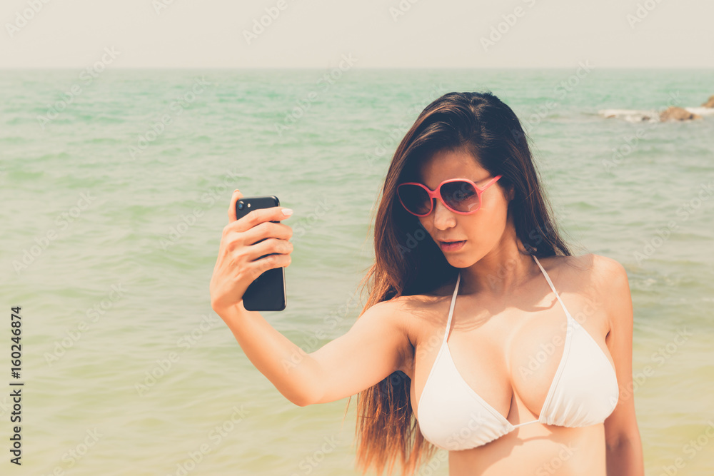 Beautiful attractive large breast asian bikini woman posing sexy portrait  on beach smart phone selfie foto de Stock | Adobe Stock
