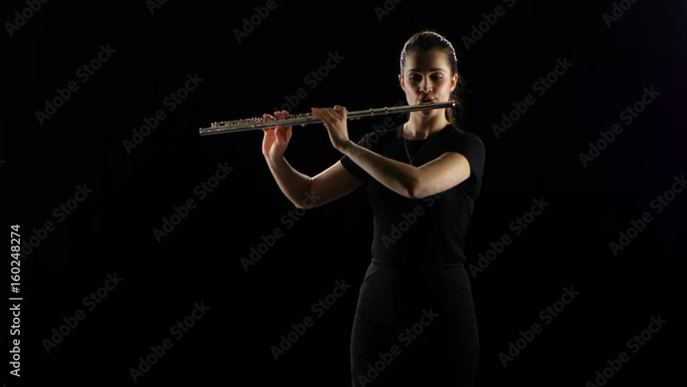 Woman plays on the flute slow melody. Black studio background Woman plays on the flute slow melody. Black studio background