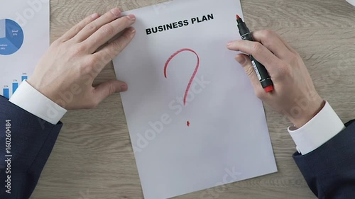 Man in suit putting huge red question mark under business plan, lack of ideas photo