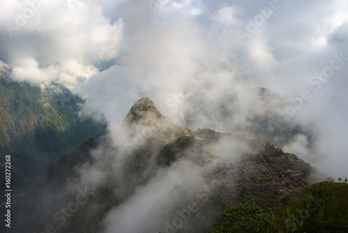 Machu Picchu illuminated by the first sunlight coming out from the opening clouds. The Inca's city is the most visited travel destination in Peru. Mist, clouds and fog covering the valley.