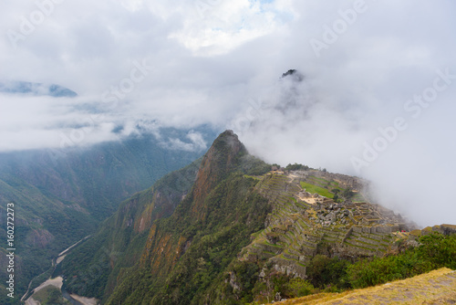 Machu Picchu illuminated by the first sunlight coming out from the opening clouds. The Inca's city is the most visited travel destination in Peru. Mist, clouds and fog covering the valley.