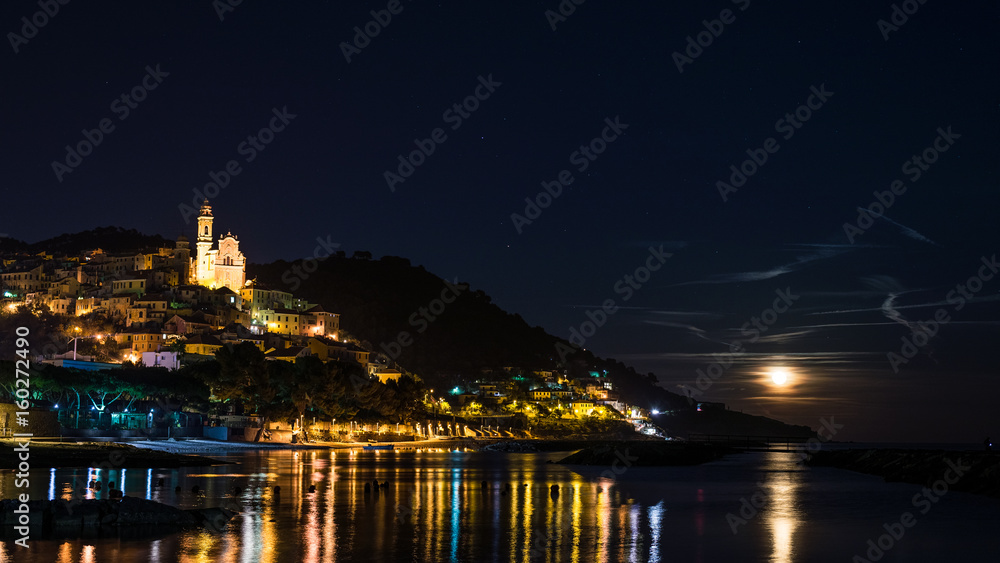 The historical town of Cervo glowing in the night under moonlight and starry sky on the coastline of Ligurian Riviera, famous travel destination in Italy.