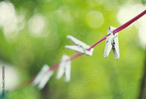 White plastic clothespins hanging on red rope with beautiful bokeh green background © liyavihola
