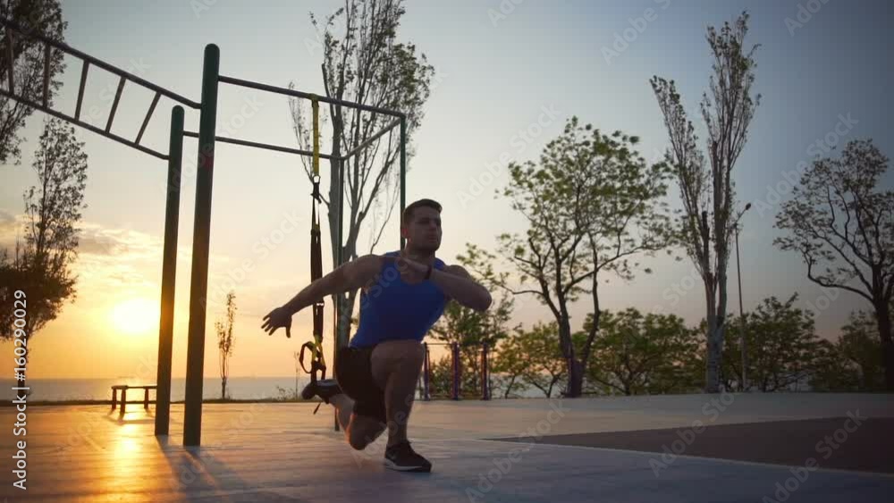 Healthy strong man engaged in trx exercises jump workout outdoor dawn slowmotion Healthy strong man engaged in trx exercises jump workout outdoor dawn slowmotion