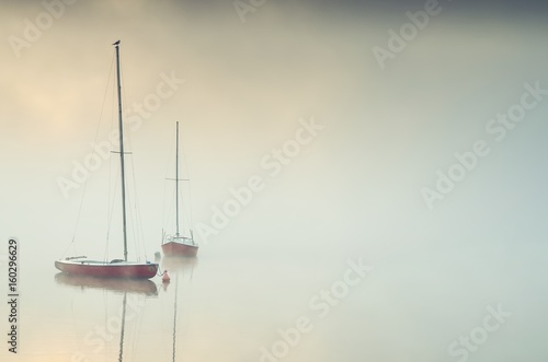 Minimalist foggy morning landscape. Boats on the lake.