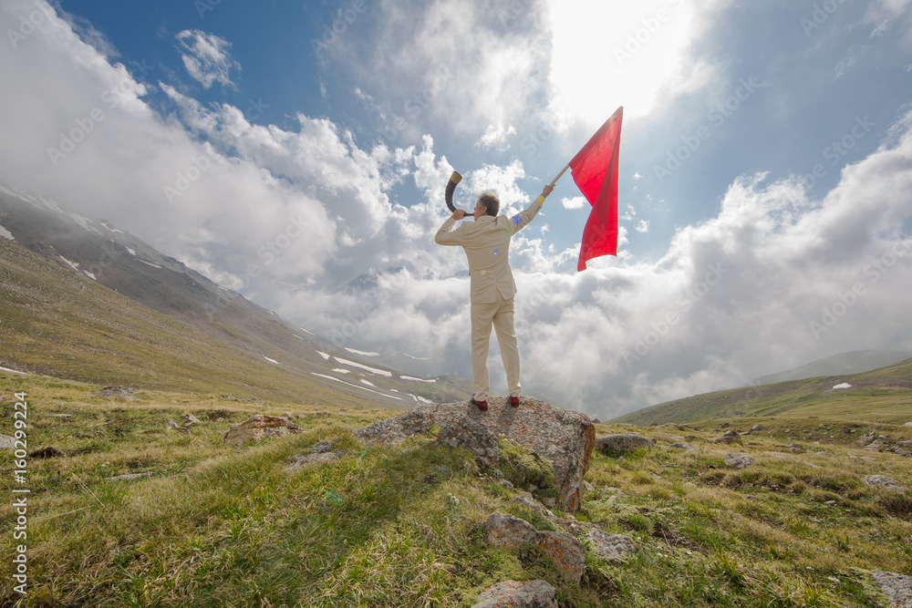 Businessman in a white suit on a mountain with a red flag