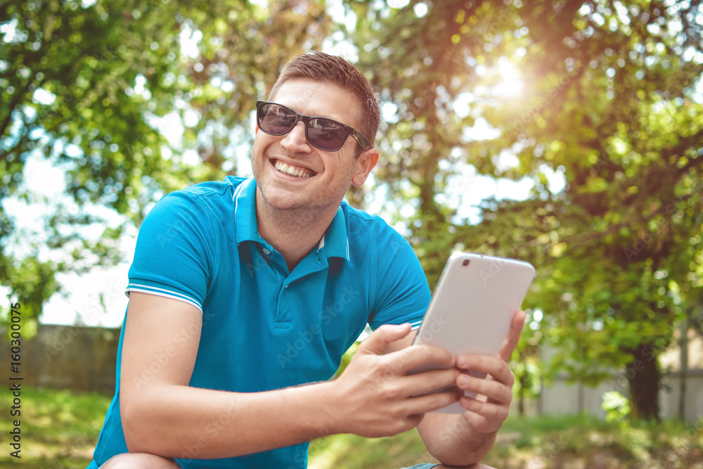 Young man using tablet on park bench on a summers day Young man using tablet on park bench on a summers day