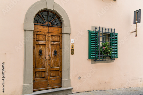 Arched wooden door next to a window with green shutters, bars, and a flowerbox.