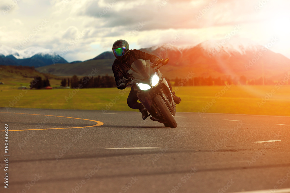 Obraz premium man riding sport motorcycle leaning in sharp curve with traveling scene background